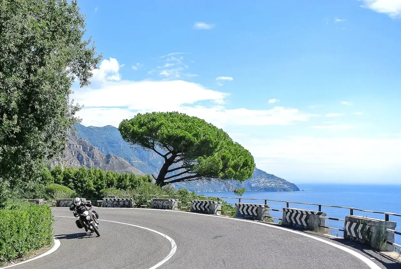 Motociclista su strada panoramica in Liguria, con mare blu e montagne sullo sfondo. Un viaggio di tre giorni indimenticabile.