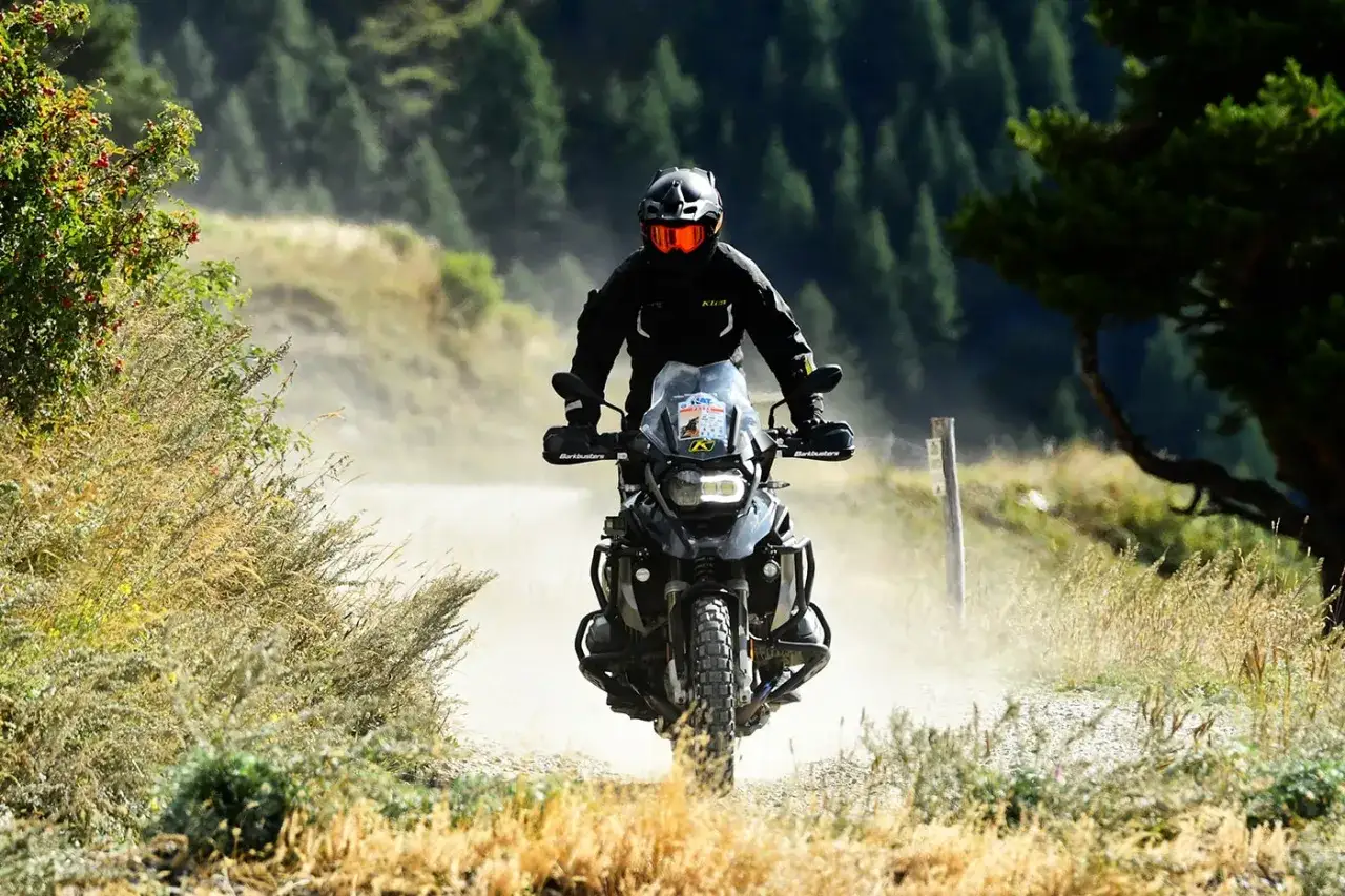 Motociclista su strade sterrate percorribili in moto in Lombardia, solleva polvere tra i boschi.