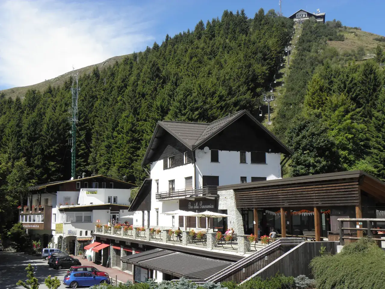 Panoramica Zegna: alberghi e ristoranti ai piedi della montagna, con seggiovia che sale tra i pini.