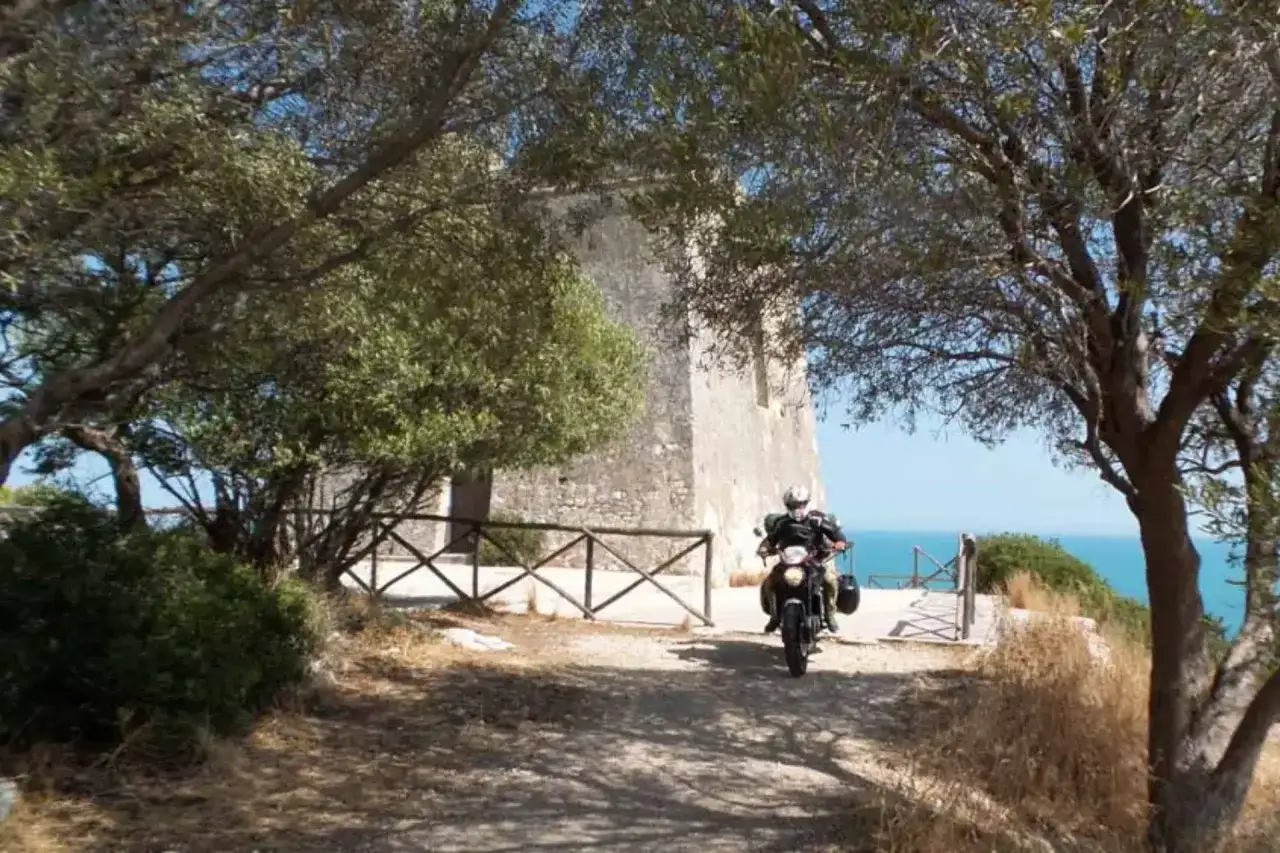 Un motociclista esplora il Gargano, passando accanto a un'antica torre con vista sul mare.