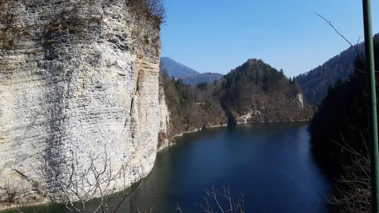 Scogliere imponenti si specchiano nelle acque scure del lago di Senaiga, circondato da boschi e montagne.
