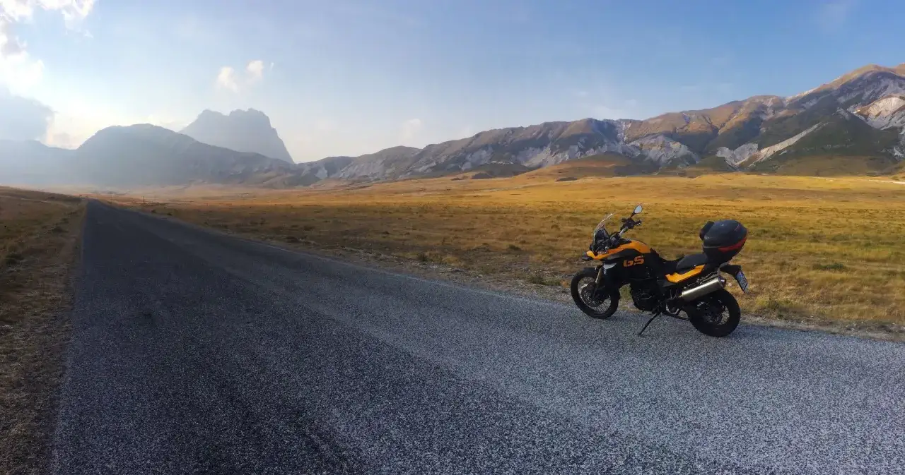 Moto gialla e nera parcheggiata sul ciglio di una strada deserta, con un vasto campo e montagne sullo sfondo. Un'avventura su due ruote nel campo imperatore moto.