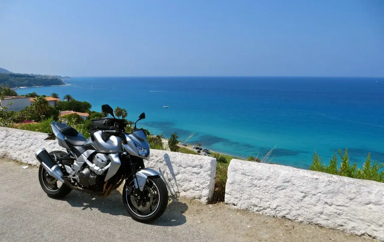 Moto d'argento parcheggiata con vista sul mare cristallino della Calabria. Un invito a esplorare la costa in moto.