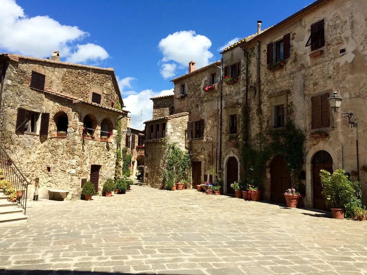 Piazza acciottolata a Montemerano, con antichi palazzi in pietra e fiori in vaso. Un luogo incantevole da scoprire.
