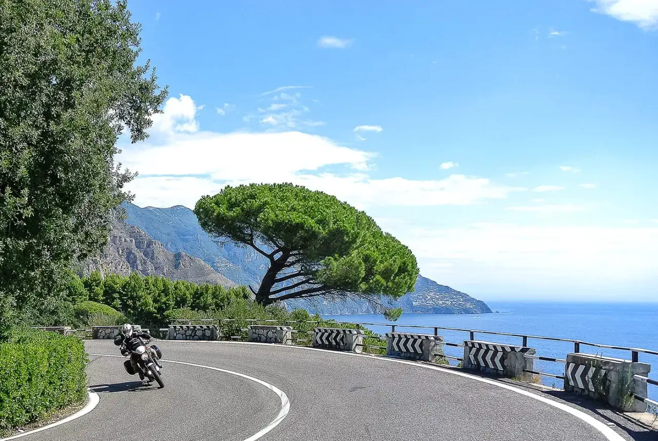 Motociclista in viaggio da Terracina a Sperlonga, su una strada panoramica con vista sul mare e montagne.