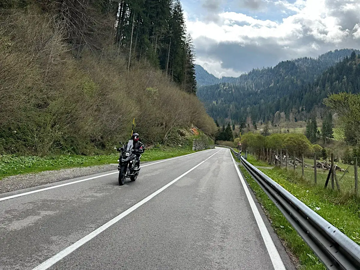 Motociclista su strada panoramica, con montagne boscose sullo sfondo. La sella Ciampigotto &egrave; pronta per un'avventura.