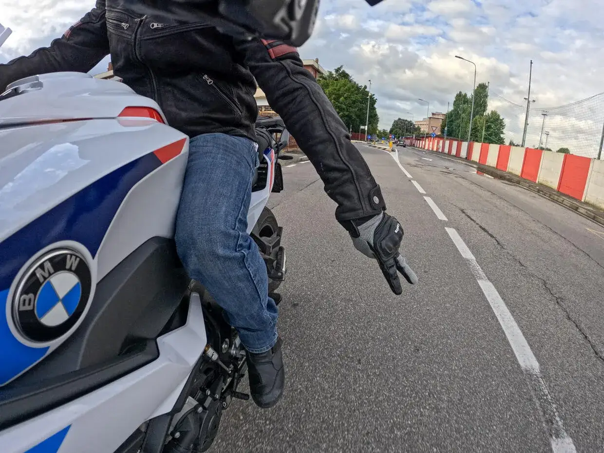 Motociclista in jeans e giacca di pelle fa il segno della V, un gesto del linguaggio motociclisti italiano, mentre sfreccia su una BMW.