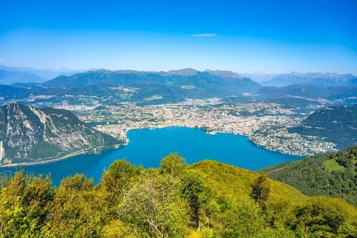Vista panoramica di un lago blu intenso con una citt&agrave; costiera e montagne sullo sfondo. Sembra il balcone d'Italia.