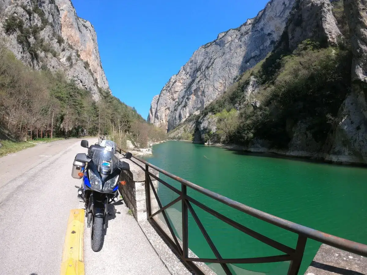 Moto parcheggiata lungo la strada panoramica delle Gole del Furlo, con il fiume color smeraldo e le imponenti pareti rocciose.