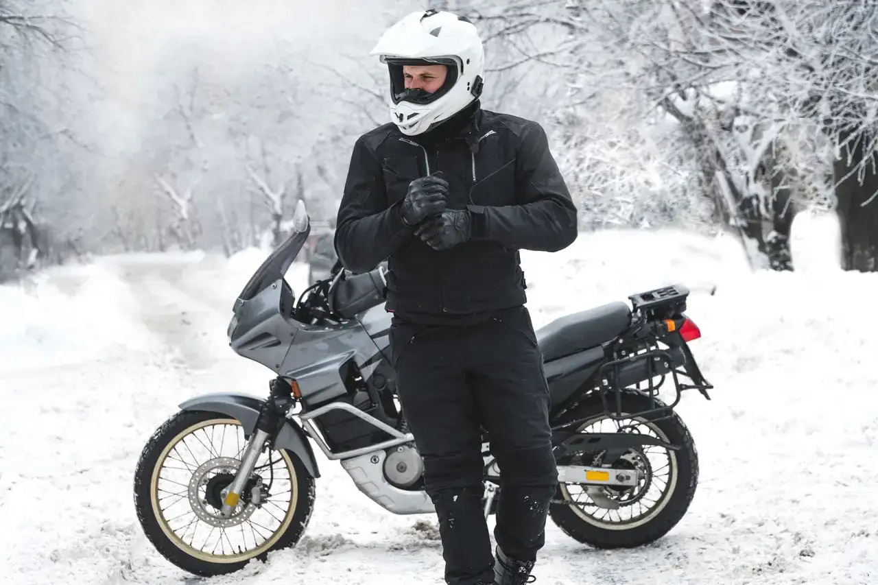 Motociclista in abbigliamento invernale, pronto per un'avventura in moto inverno su una strada innevata.