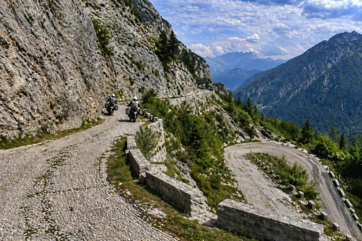 Due motociclisti percorrono una strada statale 9 via emilia tortuosa, tra montagne rocciose e verdi valli.