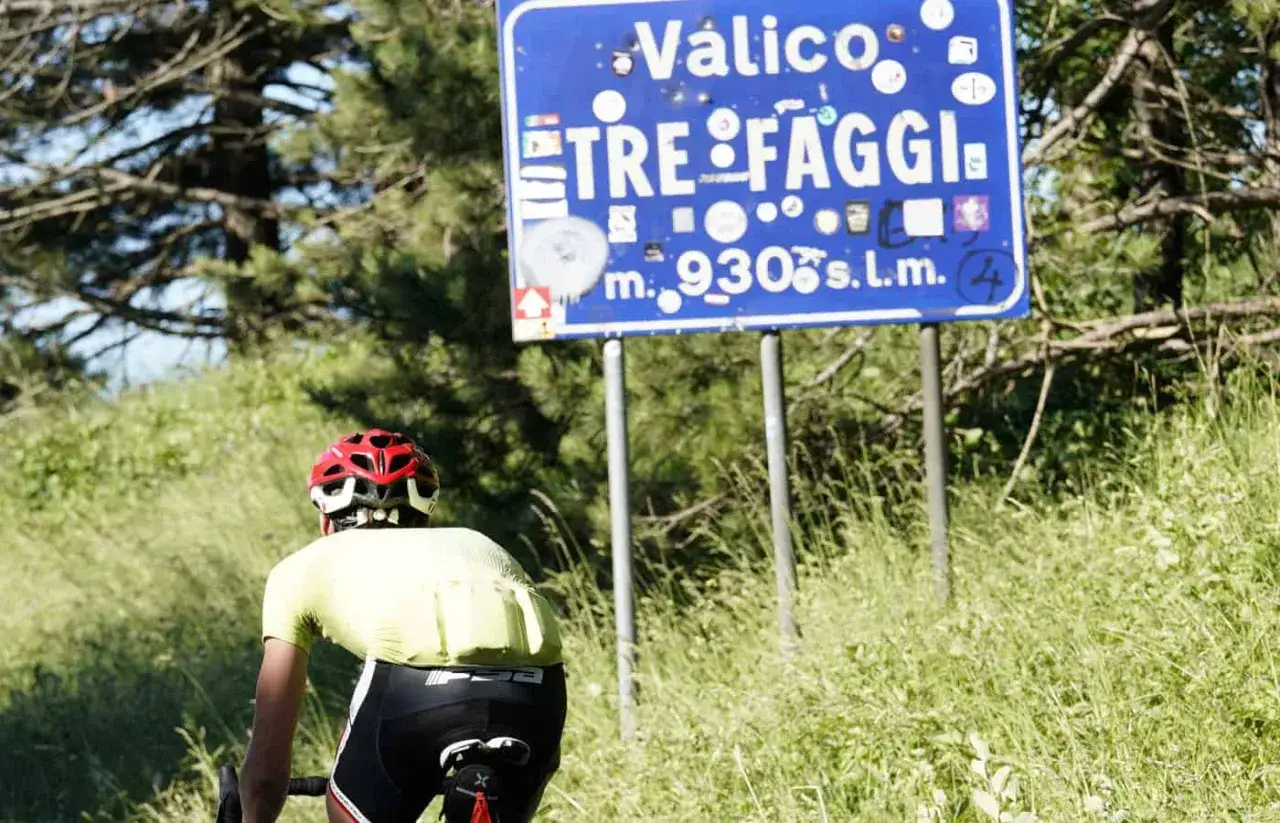 Ciclista in salita verso il valico Tre Faggi, con cartello che indica 930 metri sul livello del mare.