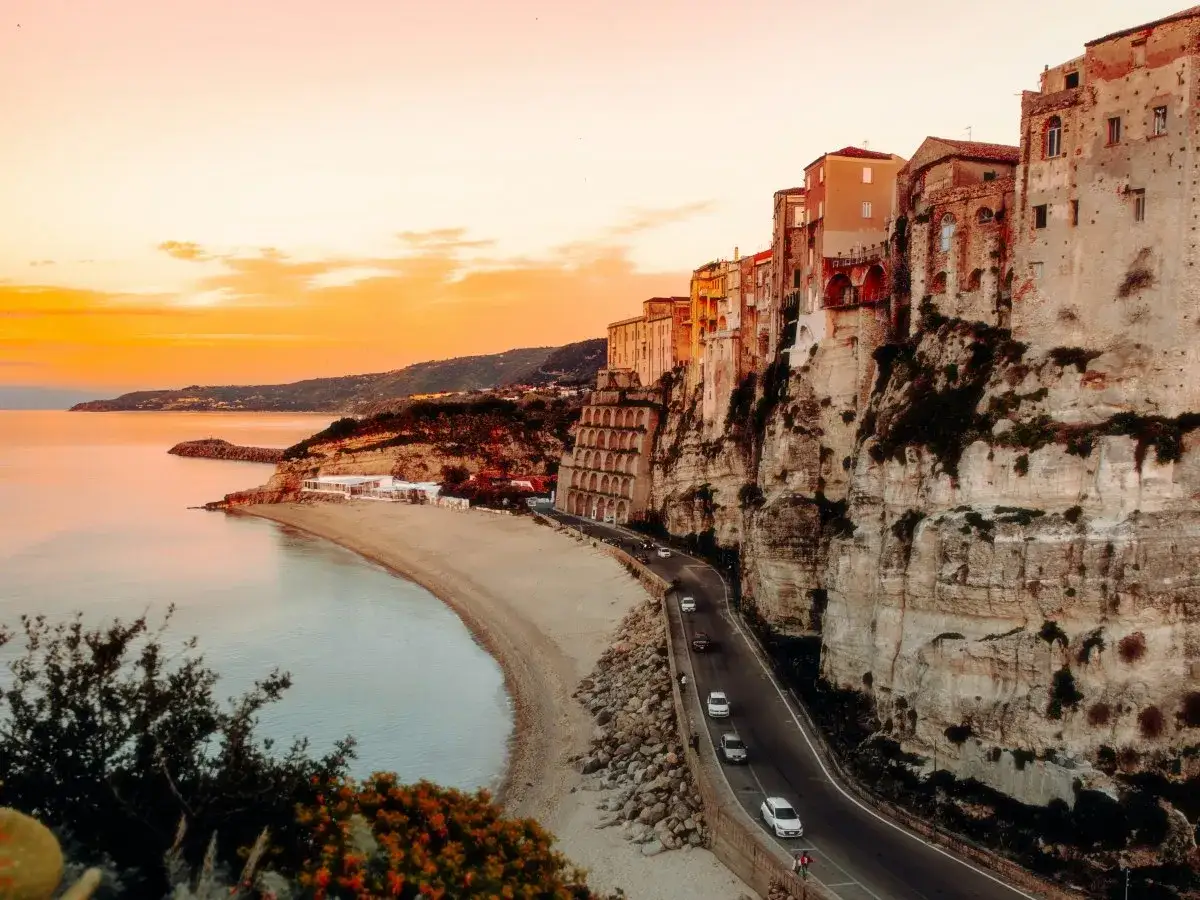 La costa della Sila in moto, con case aggrappate alla scogliera e il mare al tramonto.