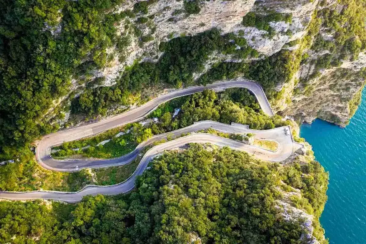 Strada della forra in moto, un nastro d'asfalto serpeggiante tra rocce e vegetazione lussureggiante, con il mare azzurro a picco.