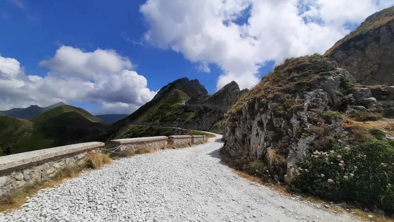 Strada sterrata in montagna, ideale per giri in moto tra Piemonte e Liguria, con rocce scoscese e cielo azzurro.