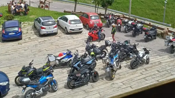 Un gruppo di motociclisti si ferma per una pausa al passo Zambla, con moto parcheggiate accanto ad alcune auto.
