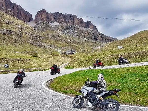 Motociclisti in gruppo affrontano le curve del passo della Cappelletta, tra verdi pendii e imponenti pareti rocciose.